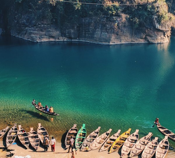Crystal-clear waters of the Umngot River in Meghalaya, surrounded by boats and rocky cliffs, offering serene natural beauty.
