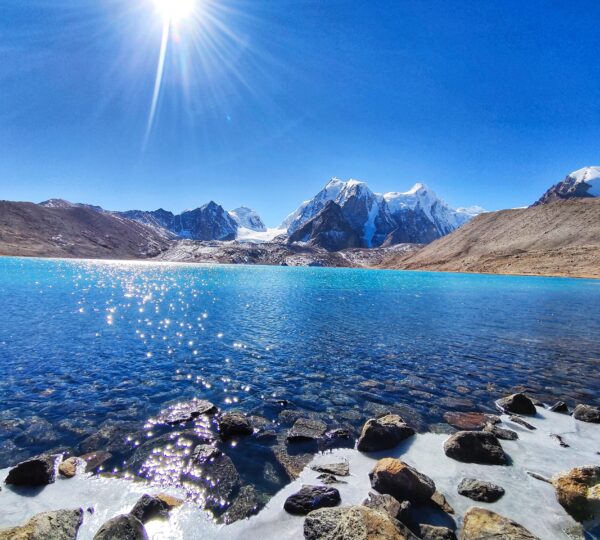 A serene lake reflecting snow-capped mountains under a bright sun in Sikkim, a must-visit destination for nature lovers and adventurers.