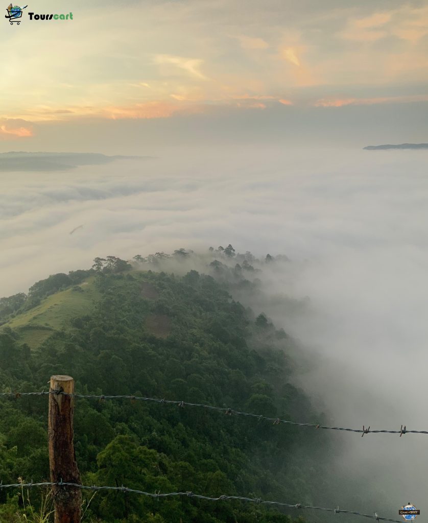 A mesmerizing view of lush green hills blanketed by clouds at sunrise, captured from a viewpoint in Meghalaya.