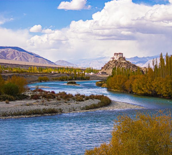 The picturesque landscape of Ladakh featuring the Indus River, barren mountains, and a traditional monastery, showcasing the region's natural and cultural charm.