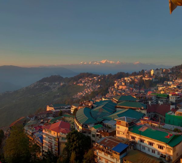 A breathtaking view of Darjeeling, the 'Queen of Hills,' featuring terraced houses, lush green landscapes, and the distant Himalayas at sunrise.