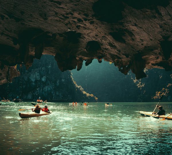 Tourists kayaking through a serene river cave in Vietnam, surrounded by dramatic limestone formations and natural light filtering through the cave opening.