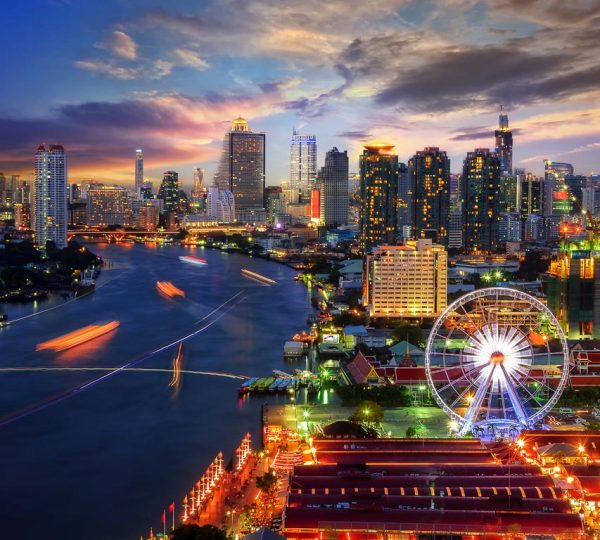 A vibrant cityscape of Bangkok, Thailand, featuring illuminated skyscrapers, the Chao Phraya River, and the iconic Ferris wheel at dusk.
